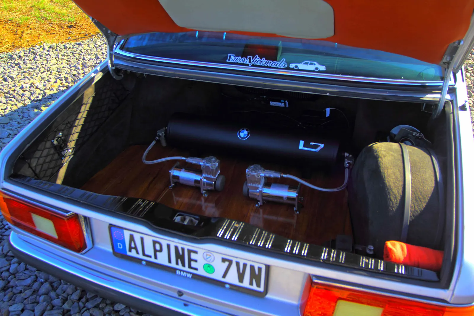 Air suspension install in a BMW E23 trunk with a BMW-branded air tank and twin chrome compressors on a wood floor