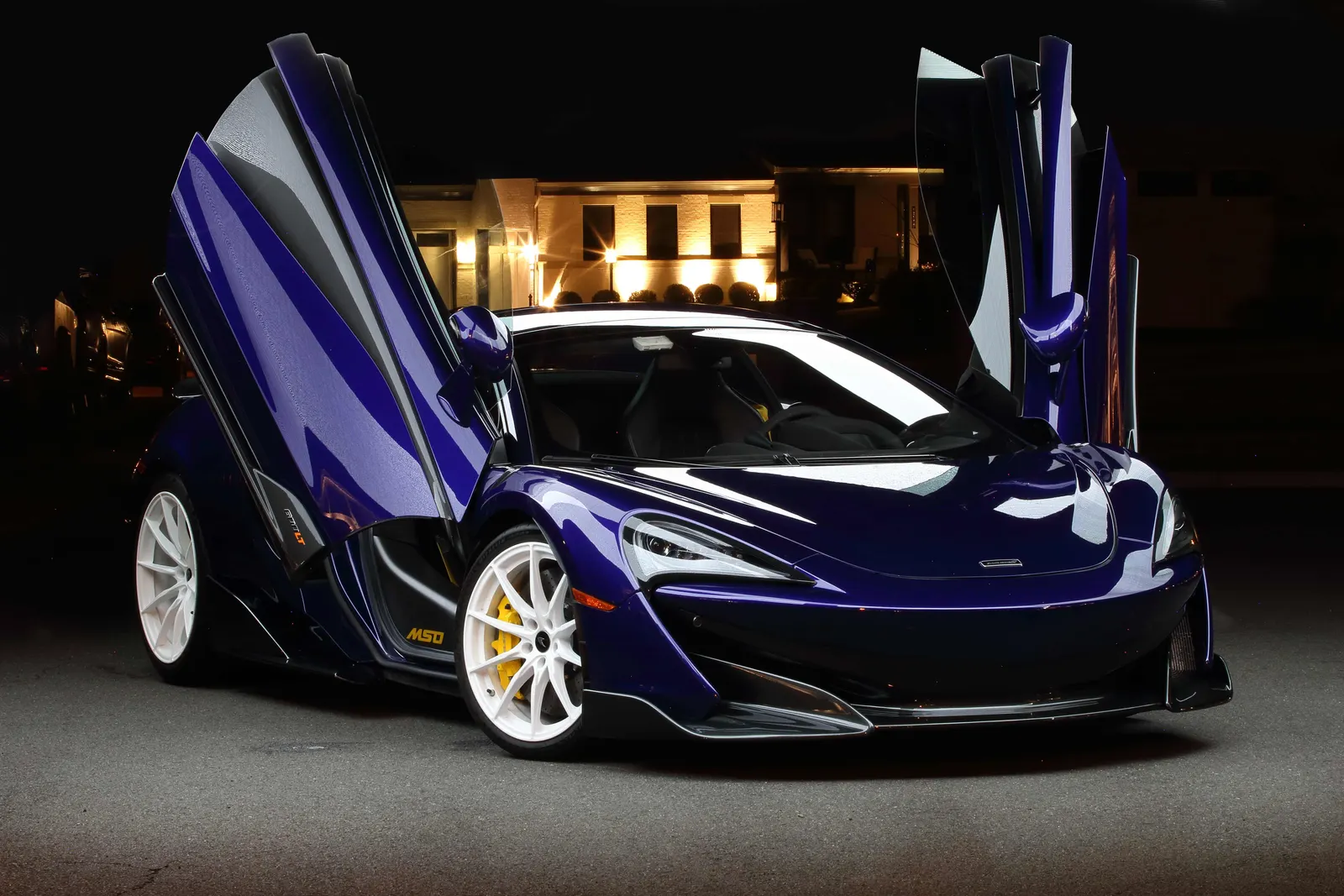 Purple McLaren 600LT with its dihedral doors raised, white wheels and yellow brake calipers, photographed at night