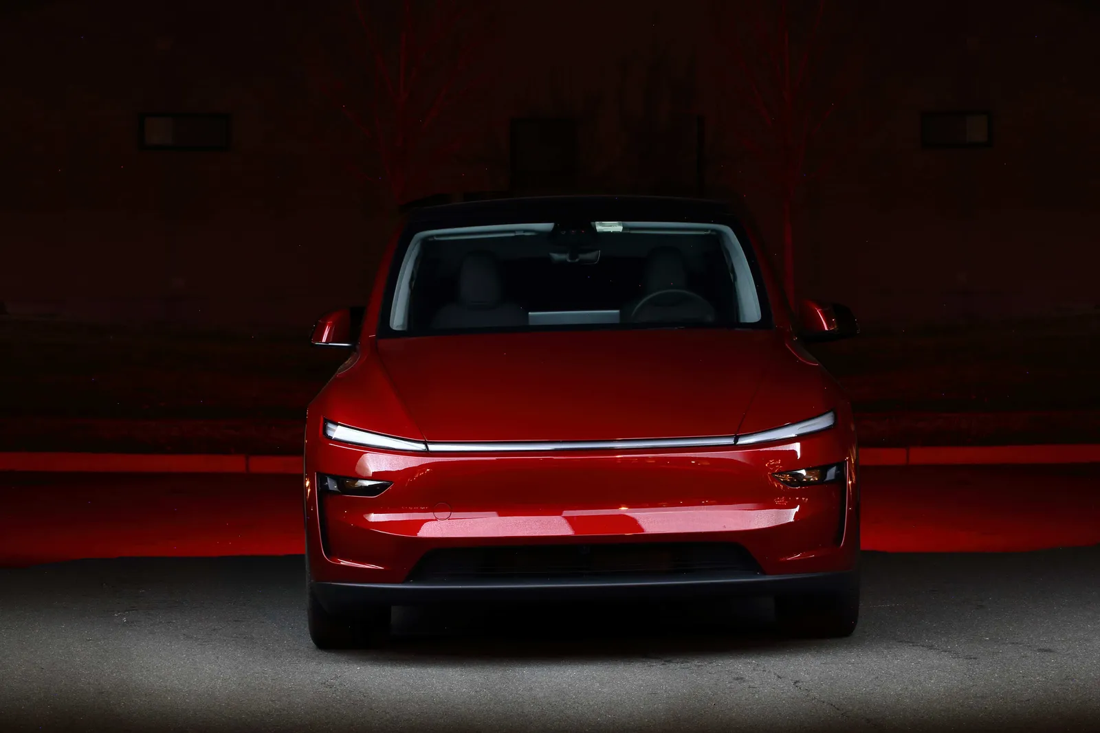 Red Tesla Model Y photographed head-on at night with its full-width light bar lit against a red-washed backdrop